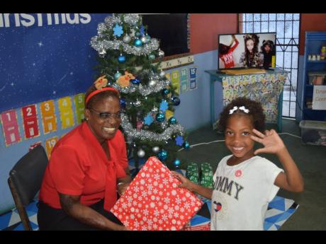 SAJ internal auditor, Jean Hinds-Bell, presents a Christmas gift to a student of the Marcus Garvey Basic School.