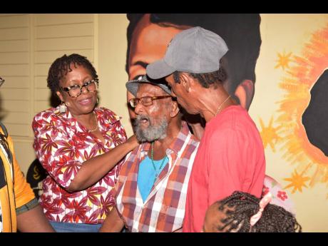 Dr Angela Brown Burke (left), member of parliament for St Andrew South West, Byron Jacques (right) comfort the nephew of Amy Jacques, 94-year-old Eric Jacques (centre), as he burst into tears as the mural of his aunt is revealed during the renaming of Jacq