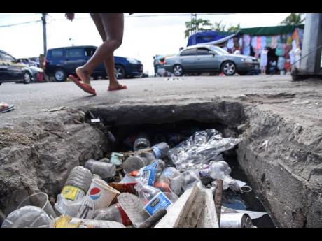 A pedestrian walks past an open manhole filled with garbage at the intersection of Burke Road and Young Street in Spanish Town, St Catherine, on Wednesday.