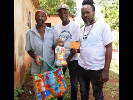 Michael Tulloch (centre), former Reggae Boy and member of the GIVE Foundation, and Enroy Thomas (right) present Neville Tulloch with a care package. The GIVE Foundation presented care packages recently to more than 90 residents in several communities in St