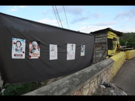A black banner bearing the images of Kemesha Wright and her four children with the message “Forever loved. Truly missed by family and friends. You left a void in our heart. We miss you!!!” hangs high in the rural community of Cocoa Piece, Clarendon. A 