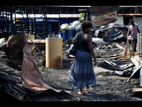 A woman walks through the rubble on Tuesday after a fire of an unknown origin destroyed a section of the Rae Rae Market in downtown Kingston on Monday night.