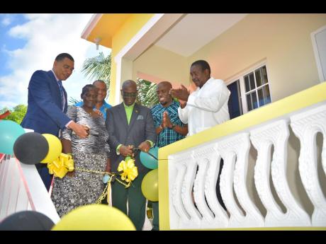 Prime Minister Andrew Holness (left) and Local Government and Rural Development Minister Desmond McKenzie (third right) cut the ribbon to officially hand over a new two-bedroom unit to Norma ‘Peaches’ Folkes (second left) in Port Maria, St Mary, on Fri