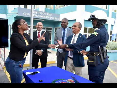 An animated Carlette DeLeon, managing director of Breakthrough Communications, receives a machine-generated demo ticket from Constable Morata Murdock at the Office of the Commissioner of Police on Old Hope Road, St Andrew, Thursday. They were joined by (fr