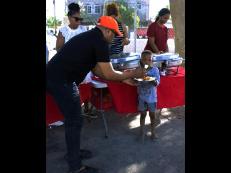 Sheldon D. Millington, chairman, House of SDM, serves a cooked meal to a child from the Torrington Park community during a recent giveback. 