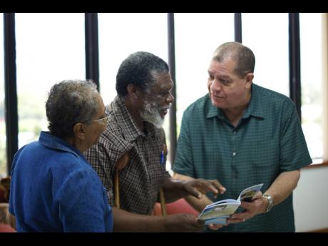 In this May 5, 2017 file photo, Minister of Finance and the Public Service, Audley Shaw (right) speaks with FINSAC victim, Mecheck Willis (centre) after he presents him with a copy of his book, ‘God is my Guide: Reform of the Mind’. Sharing the moment 