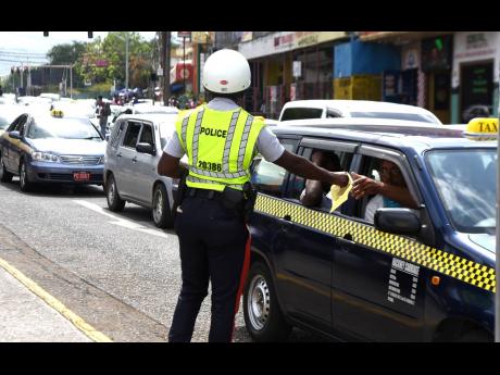 A policeman issues a traffic ticket  to a taxi operator on Hope Road, St Andrew, on May 27, 2021.