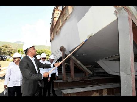 Prime Minister Andrew Holness (centre), paints a boat while looking on from left are Charles Johnston, vice-chairman of GSRJ; Peter Harren, chairman of German Ship Repair Jamaica (GSRJ); and Col Martin Rickman (right), CEO of GSRJ, at the launch of the Ger