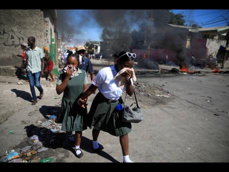 Students walk past a burning barricade that was set up by members of the police protesting bad police governance in Port-au-Prince, Haiti on Thursday.