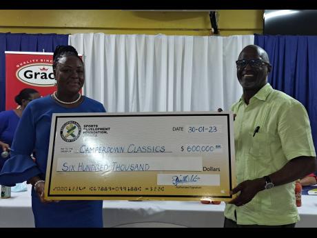 Camille Allen-Walters (left), chairperson for the Camperdown Classic organising committee,  collects  a sponsorship cheque from Sports Development Foundation general manager Denzil Wilks during yesterday’s press launch for the event at the Camperdown Hig
