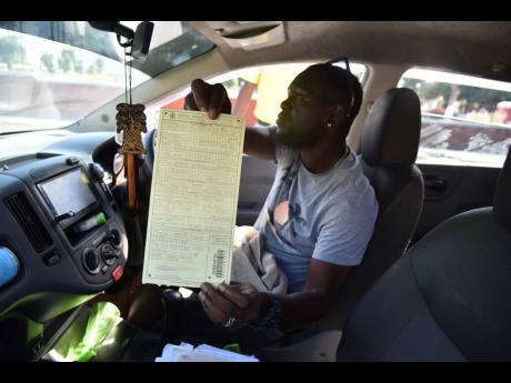 Taxi operator Ricardo Plummer shows a ticket he received for allegedly making an illegal U-turn along Orange Street in Kingston on Wednesday. The new Road Traffic Act, with heftier fees and fines, came into effect on February 1.