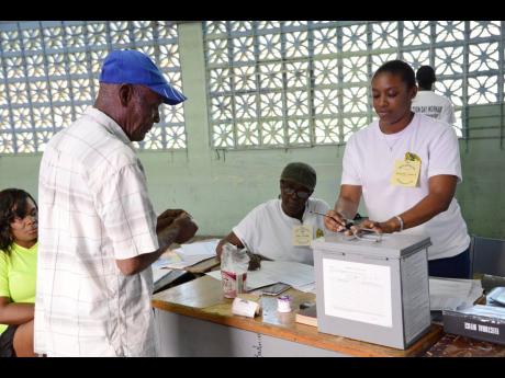 In this November 2016 photo, a voter is assisted by an official to cast his vote for the local government election at Pembroke Hall High School.