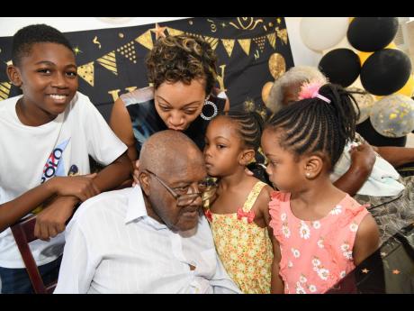 Helen Irving (second left), kisses her grandfather, Gervist Adolphus Neale, while her children (from left), Raheem, Amelia and Amirah Walters flank their great-grandfather during his 100th birthday celebration luncheon at Curphey Place on Sunday, January 2