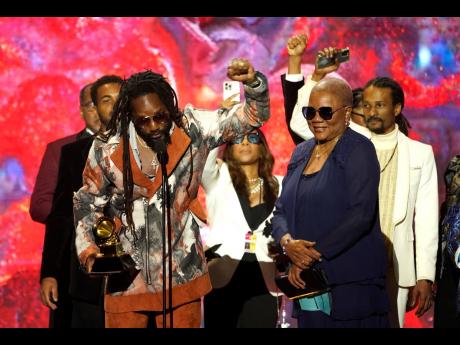 Kabaka Pyramid, left, is accompanied by his mother, Marcia Salmon, (right) and members of his management team as he accepts the award for Best Reggae Album for "The Kalling" at the 65th annual Grammy Awards in Los Angeles. 
