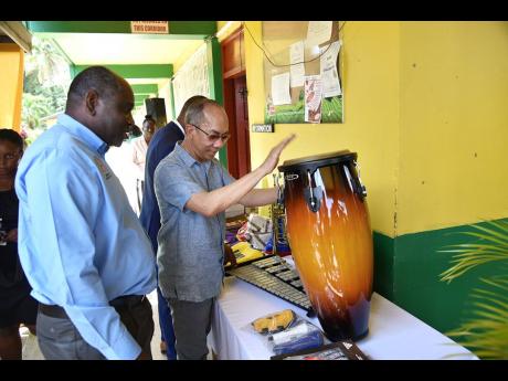 Ministry of National Security Dr Horace Chang plays a drum that the ministry donated to the Grange Hill High School in Westmoreland on Friday. Other pieces of musical instruments were also donated to the school. Permanent Secretary Courtney Williams looks 