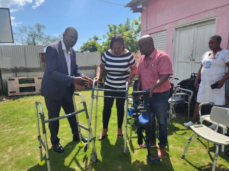 From left:  People’s National Party Councillor of the Sheffield Division and Principal of Little London High School, Garfield James, explains how the walkers bought for residents of the Savanna-la-Mar Infirmary are set up to Kenya Keddo Laing and her hus