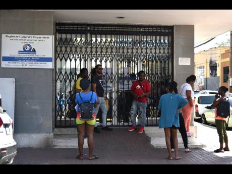 Persons stand outside the Registrar General’s Department (RGD) office at 58 Duke Street in Kingston on Monday. RGD offices were closed after dozens of employees called in sick over a compensation grievance.