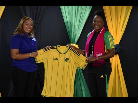 Brittany Roberts (left), marketing coordinator at Wata, receives a new Jamaica home jersey from JFF administrator Tamecia Grey during the local launch of the organisation’s partnership with Adidas at its headquarters on Tuesday.