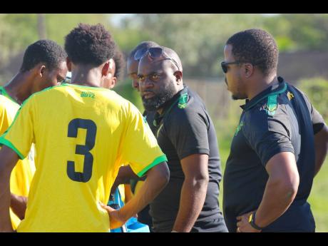 Jamaica under-17 football coach Merron Gordon (centre) addresses players during a  warm-up match against  Vere United last month. Assistant coach Andrew Peart (right) looks on.