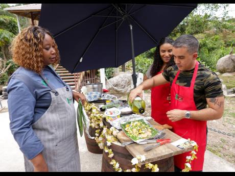 Chef Simone Walker-Barrett (left) gives Jason Dear a few tips, as he prepares his fish wrapped in banana leaves for the flame as Sainte-Marie Stephenson looks on.