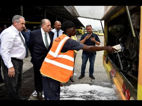 From left;  Paul Abrahams, managing director of the JUTC; Audley Shaw, minister of Transport and Mining;  Cecil Thoms, corporate communication manager;  and Alvaro Calvo, chief executive officer at IFR Labs watch as Courtney Moffatt, uses water to remove t