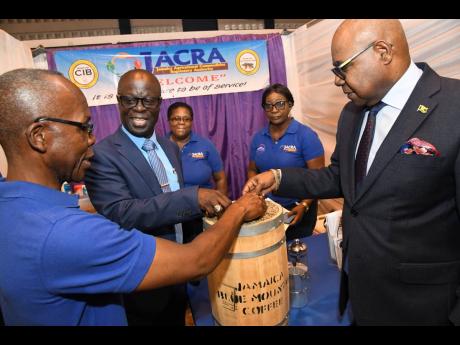 Hervin Willis (left), senior director of coffee at Jamaica Agricultural Commodities Regulatory Authority (JACRA), shows coffee beans to Tourism Minister Edmund Bartlett (right) and Winston Simpson (second left), acting CEO of RADA, while administrative ass