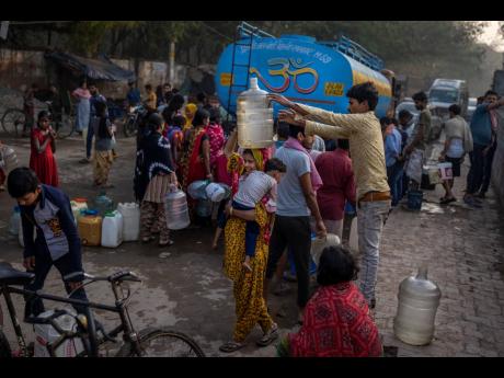 A woman balances a water can on her head while carrying a child as people collect water from a mobile water tanker on World Water Day in a residential area in New Delhi, India yesterday.