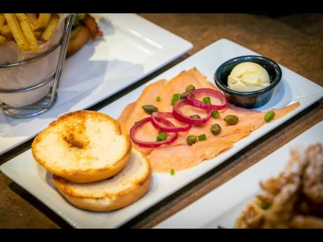Smoked salmon is served with a plain bagel with cream cheese, red and green onions and capers.