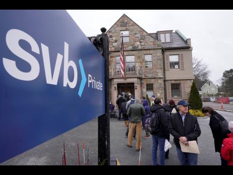 Customers and bystanders form a line outside a Silicon Valley Bank branch location on Monday, March 13, 2023, in Wellesley, Massachusetts, following its takeover by federal authorities on March 10.