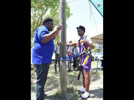 Demar Nelson (left), demonstrator for telecommunications at HEART College of Construction, gives climbing tips to Ascot High School student Dejanae Pottinger after she was fitted with a harness during the open day event on Wednesday.