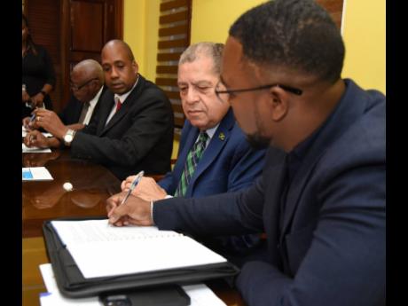Rockey Wood (right), CEO of Mineral Agency for Retail and Logistics (MARL), signs the agreement as Transport and Mining Minister Audley Shaw (second right), and Ryan Parkes, (second left), chairman of the Jamaica Railway Corporation (JRC), look on. The occ