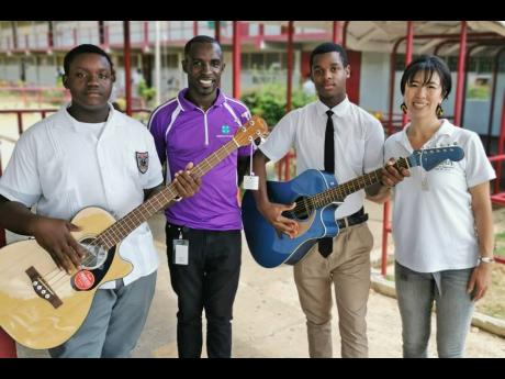 Javion Brown (left) and Ayelo Parke (second right), students of Aabuthnott Gallimore High School, try out instruments donated by Kaeru, a reggae recording studio in Japan, as Japanese volunteer Natsumi Nagamura (right) and Tedroy Gordon of Jamaica 4-H Club