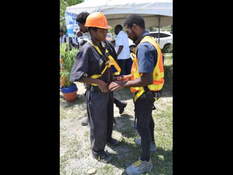 Oral Brown (right), of the General Construction Department at the HEART College of Construction Services, shows Tayla Davis, a student at Portmore College of Construction, how to put on a climbing harness during the HEART/NSTA Trust HEART College of Constr