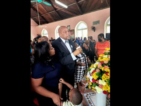 Cedric Stewart broke down in church during his mother Ena Stewart’s thanksgiving service. He gets support from his wife Chinan and son Cairo.