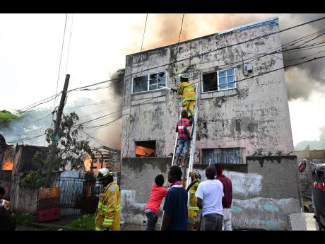 Firefighters try to prevent the raging flames from spreading to a nearby building as a multifamily dwelling is consumed by fire on Tex Lane in Central Kingston on Wednesday. At least 15 people were left homeless.