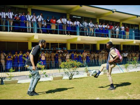 Deno Crazy and a student from Ewarton High enjoy a kickabout on the school lawn.