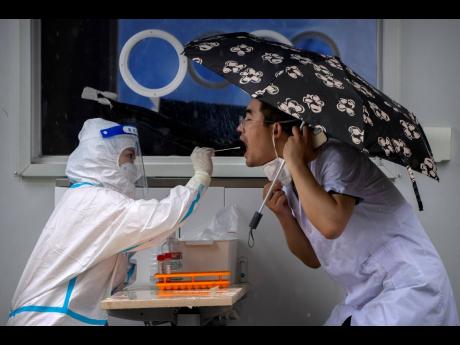 A worker wearing a protective suit swabs a man’s throat for a COVID-19 test at a coronavirus testing site in Beijing, on June 22, 2022. The World Health Organisation said yesterday that COVID-19 no longer qualifies as a global emergency, marking a symbol
