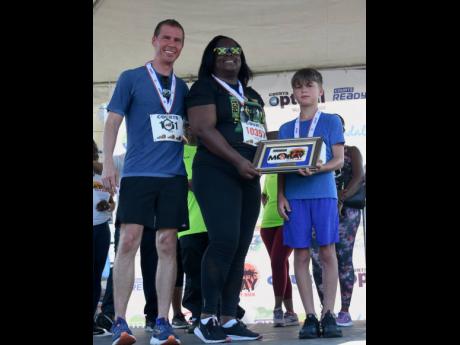 Executive Chairman of Sandals Resorts International Adam Stewart (left), and son Aston presenting the Jill Stewart 10K Run award to the Passport, Immigration and Citizenship Agency’s Tracy-Ann Patterson, who collected on behalf of Delly Vassell. The awar