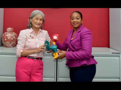 Founder and former CEO of Island Grill, Thalia Lyn, passes the chicken to new CEO Tania Waldron-Gooden, symbolising the transition to a new leader of the fast food chain, at Island Grill headquarters in Kingston on May 9, 2023. Waldron-Gooden became CEO on