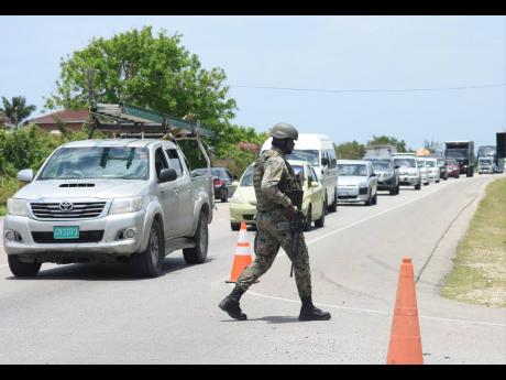 A Jamaica Defence Force [JDF] soldier walks at a checkpoint at Wiltshire in Greenwood, St James yesterday, amidst a traffic pile-up.