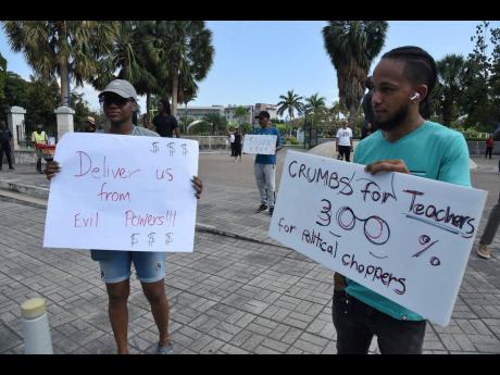 Placard bearing demonstrators outside Emancipation Park in New Kingston yesterday protest this week’s announcement of a massive salary increase for members of the political directorate. 