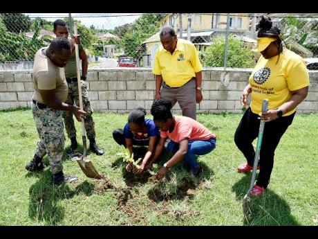 Deborah Dawes and Arrian Patman, contestants in the Westmoreland Festival Queen Competition, share in planting one of the many fruit trees that will surround the playground at New Hope Primary and Junior High School. Members of the Jamaica Defence Force, M