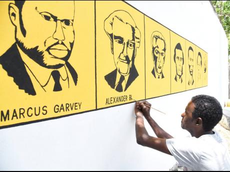 Muralist Howard Ferguson adds names of the national heroes after painting pictures on a wall at the August Town Primary School in St Andrew on Labour Day.
