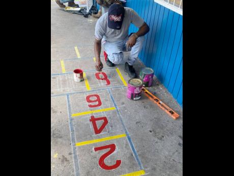Sign artist Jomo Campbell repaints the hopscotch drawing at the 
St Margaret Mary Basic and Prep School.