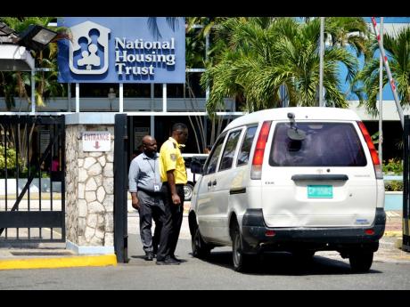 A security officer addresses an occupant of a vehicle at the entrance of the National Housing Trust’s head office in Kingston yesterday. Some employees of the  company staged a sick-out in protest of issues related to job evaluation.