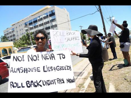Kay Osborne (left) and other demonstrators bear placards as they protest the massive salary hike for the political directorate across the street from the Ministry of Finance and the Public Service in Kingston.