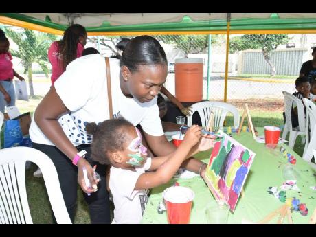 JMMB’s Jody Henry helps a little girl to finalise her artwork during the community outreach initiative hosted by Project STAR at Breezy Castle in downtown Kingston recently.