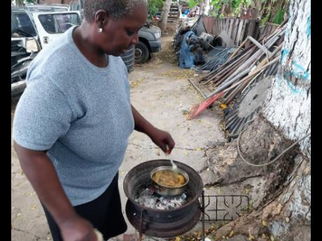 Lamour Pinnock tends to a pot of curried chicken neck and foot being cooked on a coal stove in the shade of a guango tree in the upscale housing scheme of Portmore Pines, in St Catherine.