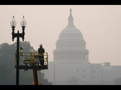 Workers finish tending a street lamp as smoke from Canadian wildfires obscures the view of the US Capitol Building in Washington yesterday.