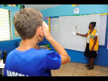 Yvonne Lewars (right), conducts an eye screening test on sixth grader Liam Rickman at  the Kiwanis Club of New Kingston Children’s Health Screenings at Liguanea Prep School in St Andrew on Thursday.